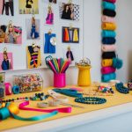 A table with colorful beads, ribbons, and tools for making DIY accessories. A mood board with trendy fashion images hangs on the wall